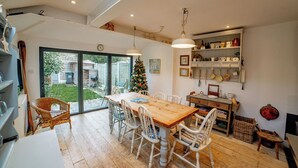 Zona pranzo con tavolo in legno e sedie bianche, un albero di Natale e una cucina con ripiani.