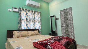 A bedroom with a bed, an air conditioner, a mirror, and a window with patterned curtains.