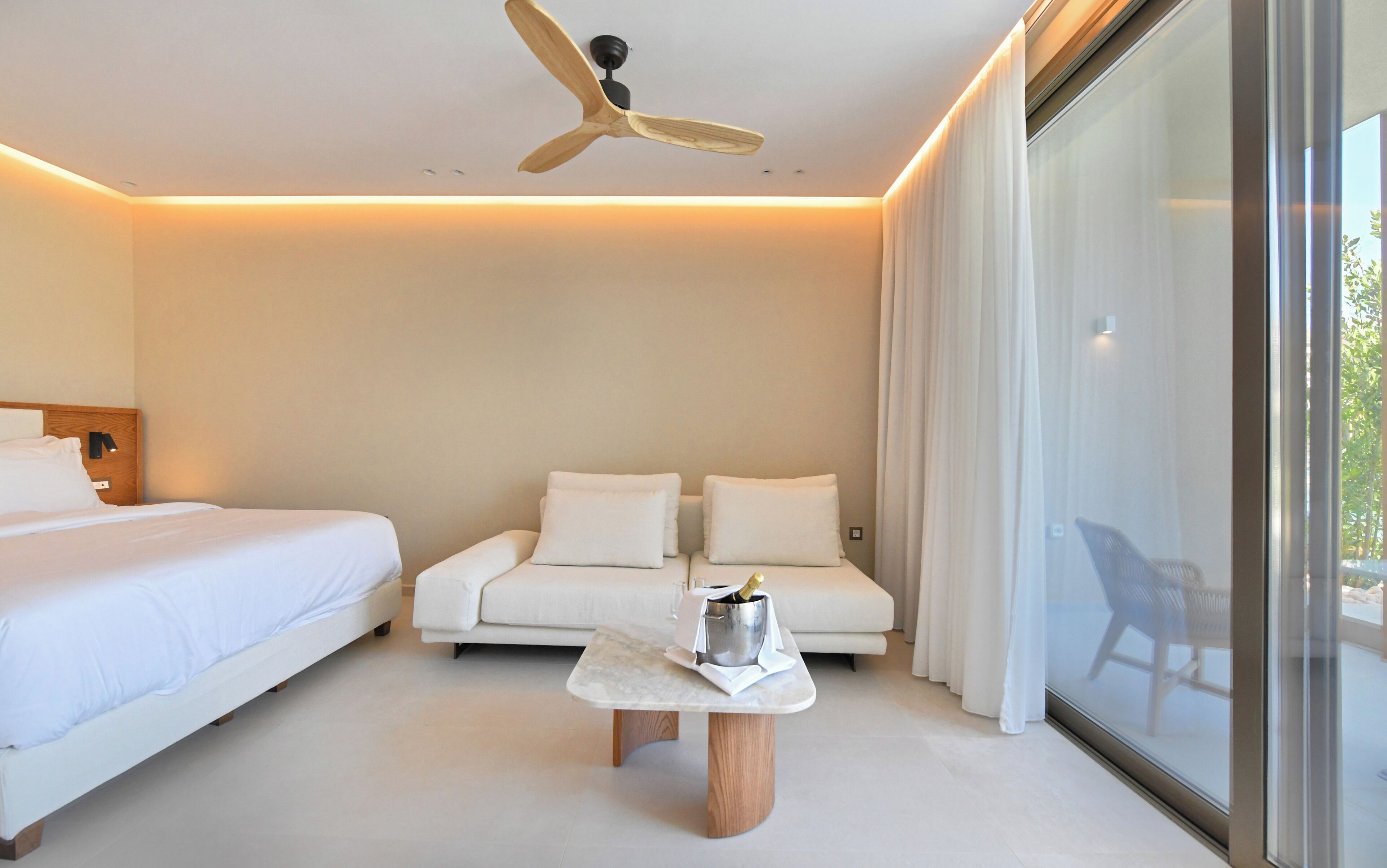 Una habitación de hotel moderna con una cama, un sofá, una mesita con una botella y un ventilador de techo.