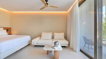 Una habitación de hotel moderna con una cama, un sofá, una mesita con una botella y un ventilador de techo.