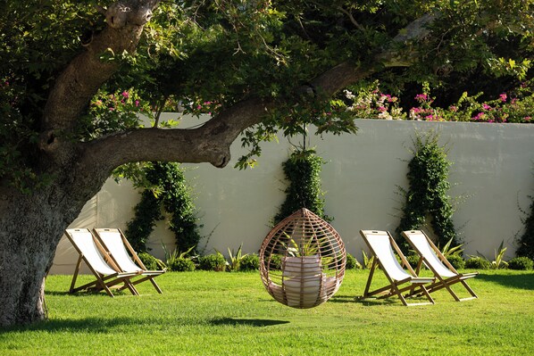 A garden with a tree, a hanging chair, and two lounge chairs.