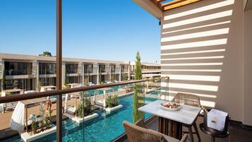 A rooftop pool area with lounge chairs and a table, overlooking a pool and a building with multiple balconies.