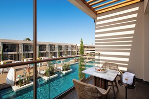 Un área de piscina en la azotea con sillones y una mesa, con vistas a una piscina y un edificio con varios balcones.