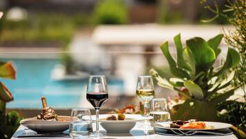 A dining table with plates of food, glasses of wine, and a pool in the background.