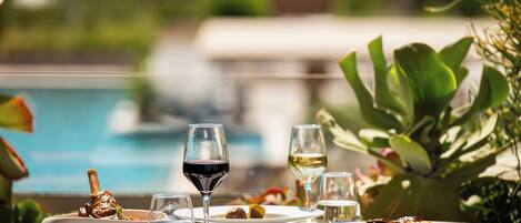 Una mesa de comedor con platos de comida, copas de vino y una piscina al fondo.