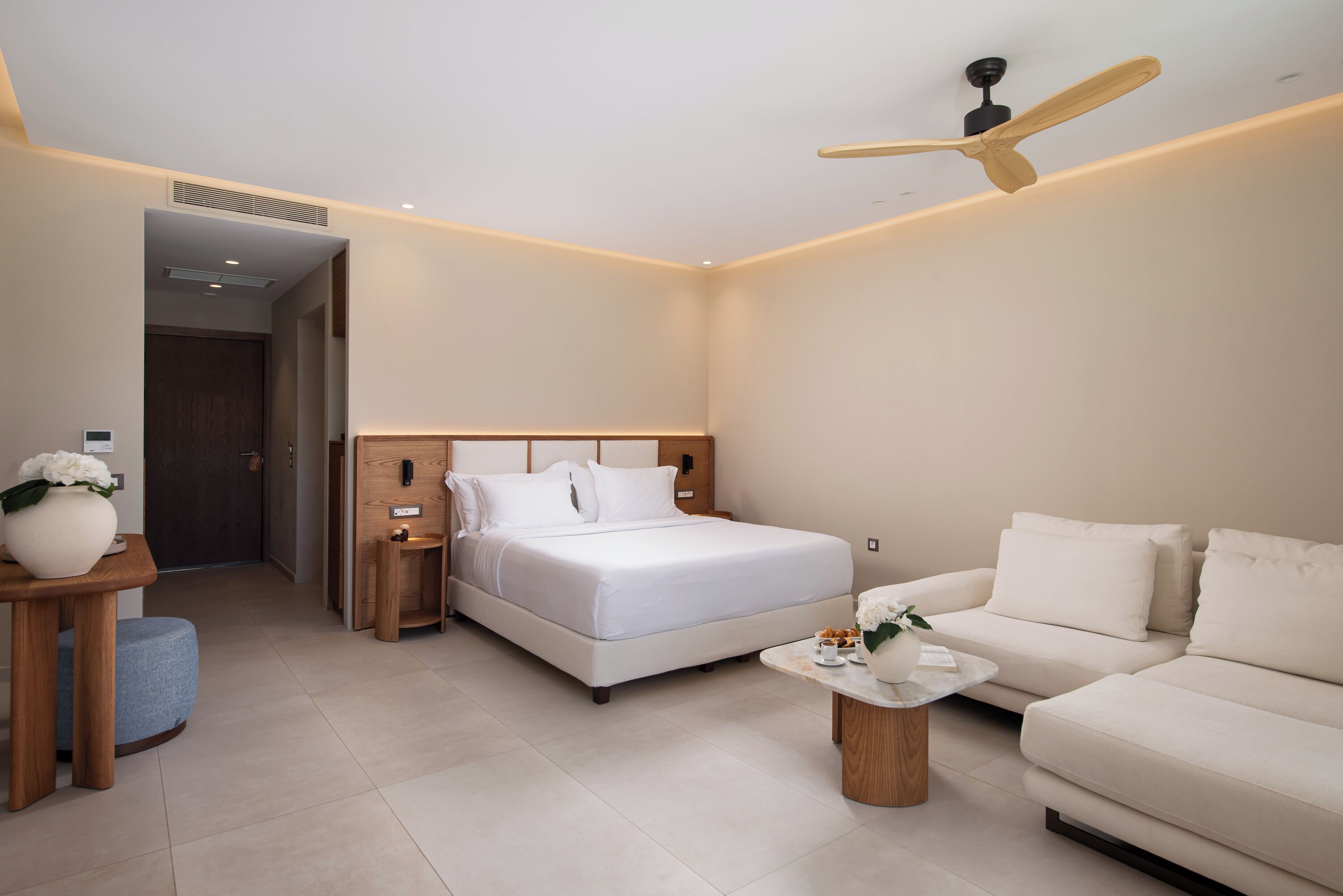 A modern hotel room with a bed, a sofa, a coffee table, and a ceiling fan.