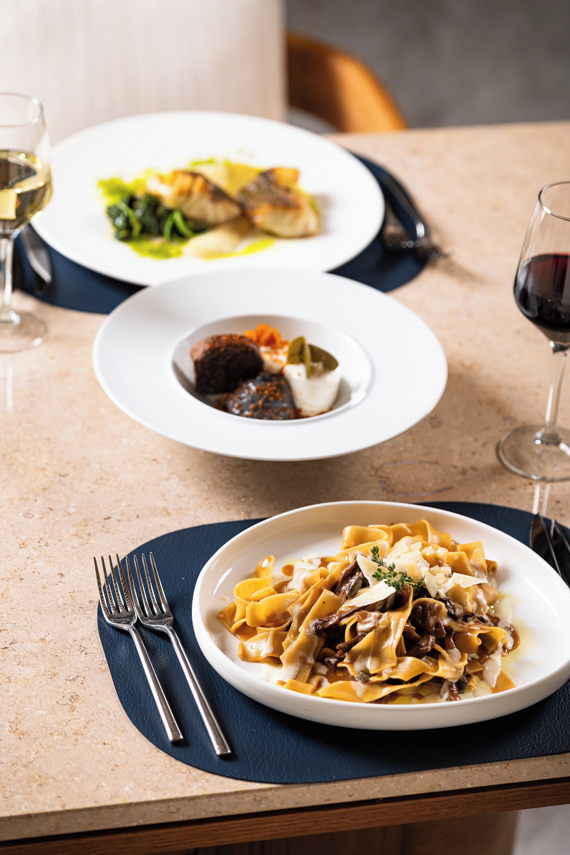 A dining table with two plates of pasta and a glass of red wine.