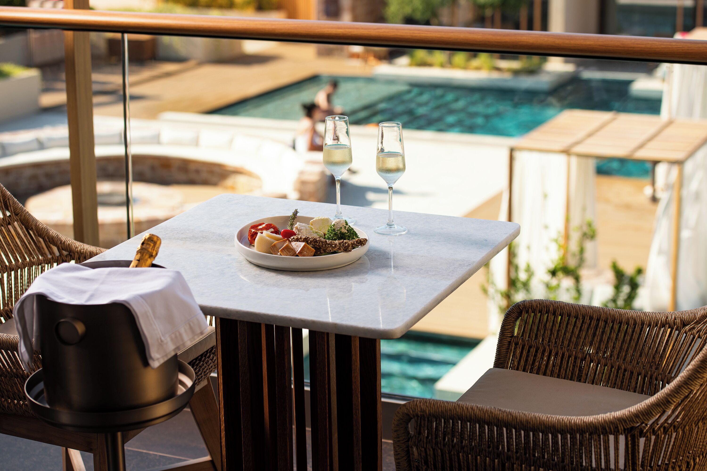 Una mesa de comedor con un plato de comida y dos copas de vino blanco, con vista a una zona de piscina.