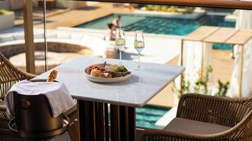 Una mesa de comedor con un plato de comida y dos copas de vino blanco, con vista a una zona de piscina.