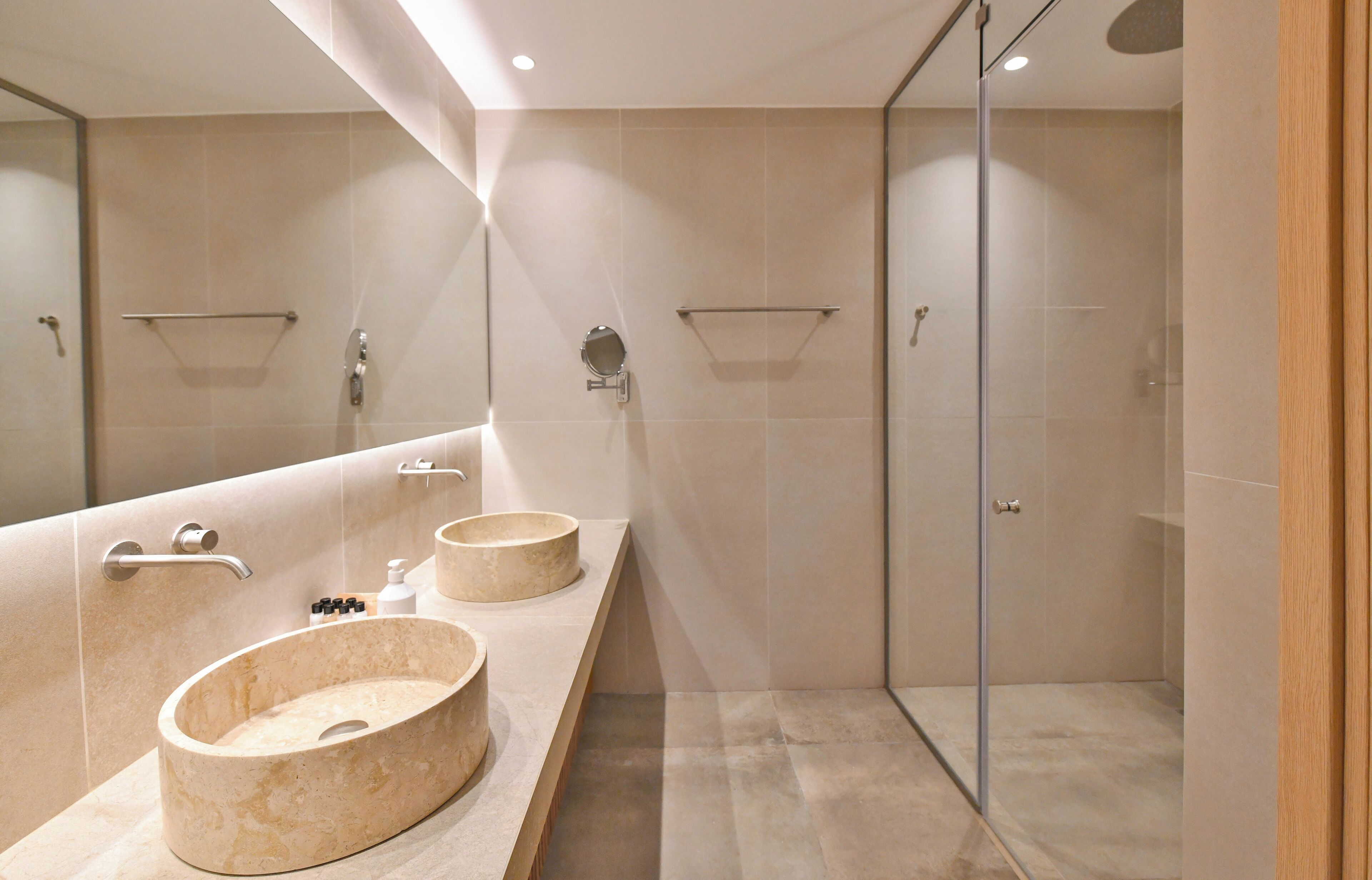 A modern bathroom with two oval sinks, a glass shower enclosure, and a large mirror.