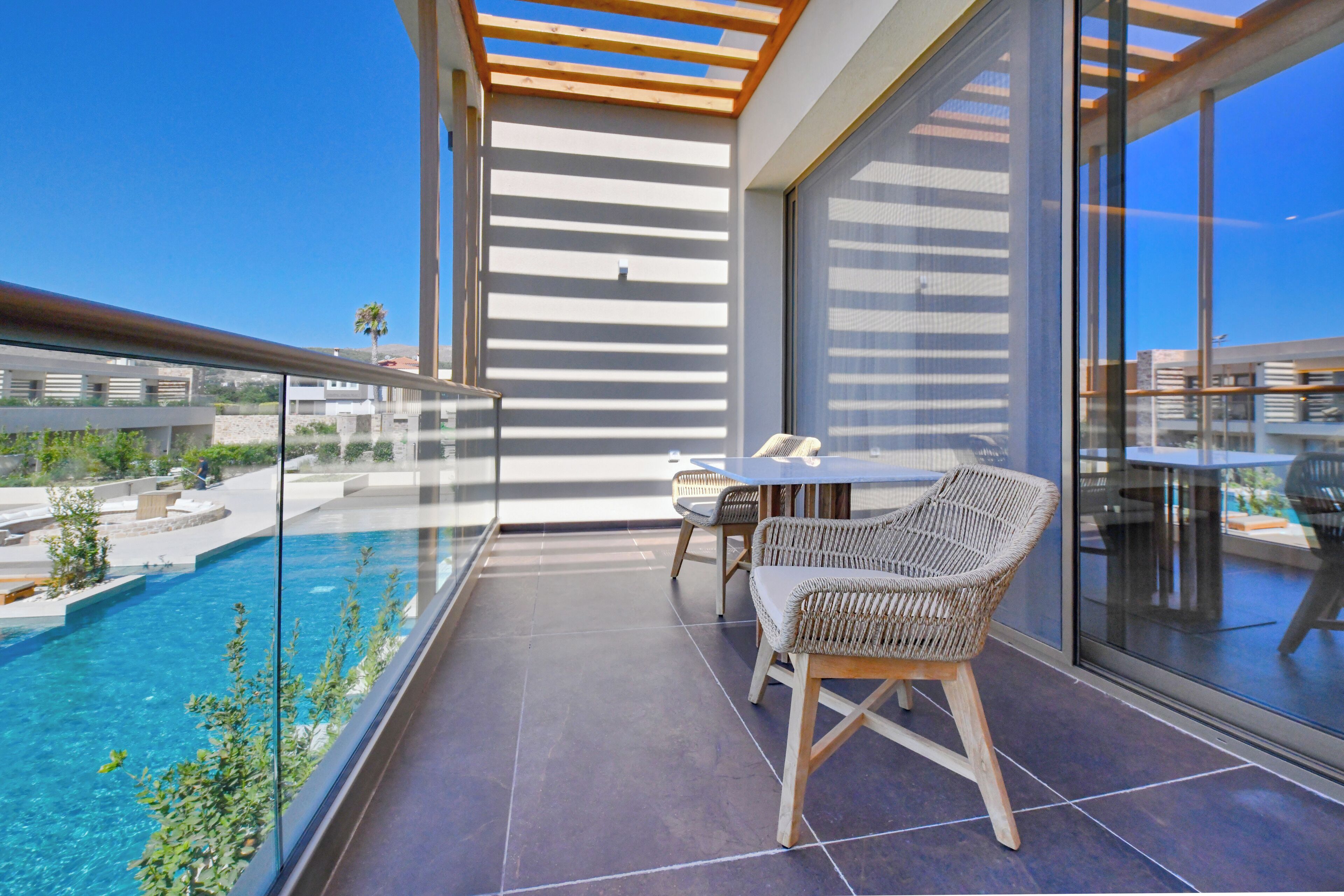 A balcony with a glass railing, a pool, and wicker furniture.