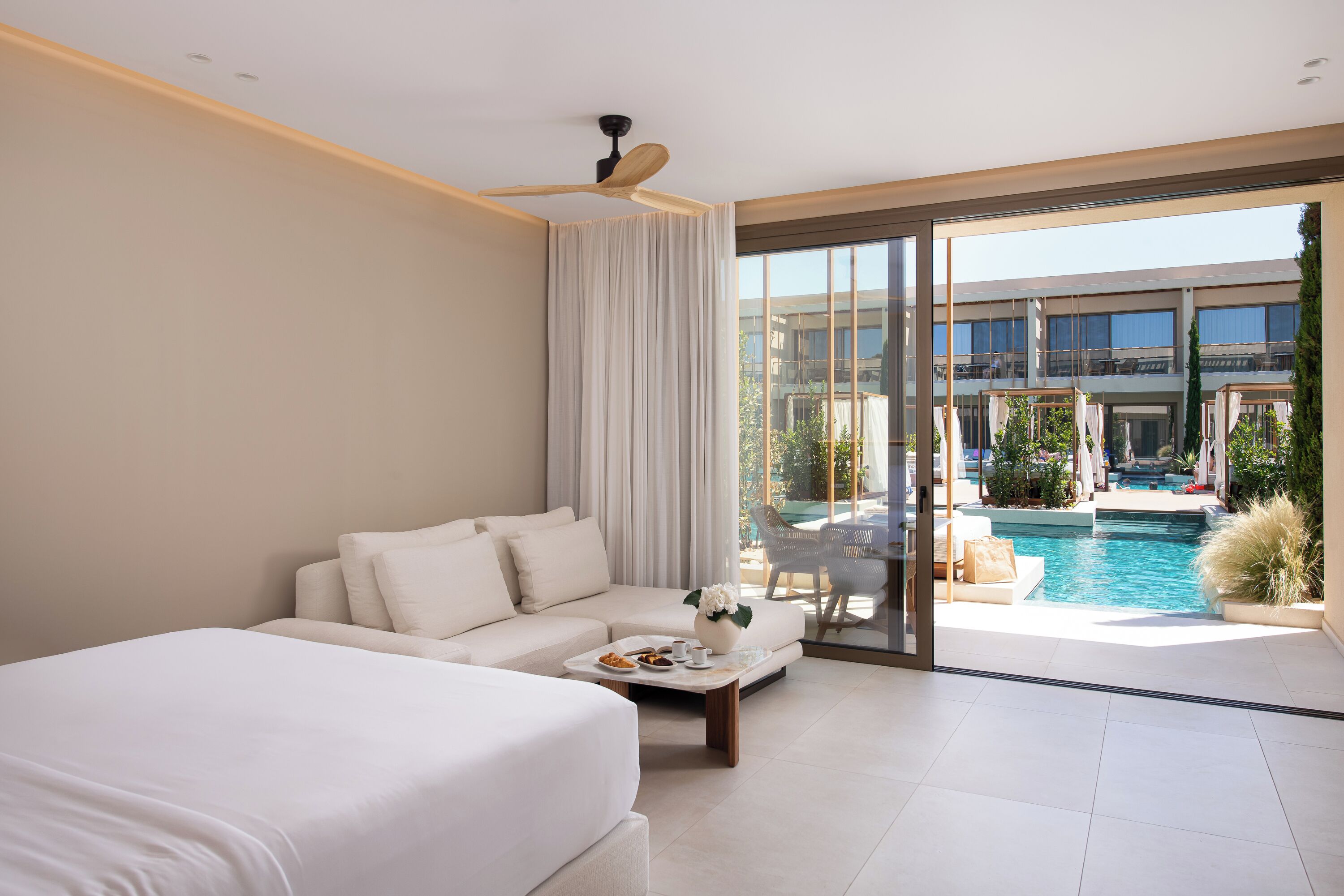 Una habitación de hotel moderna con una cama grande, un sofá, una mesa de centro y vistas a una piscina al aire libre.