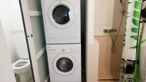 A compact laundry area with two stacked washing machines, a toilet, and a shower with a green leaf-patterned curtain.