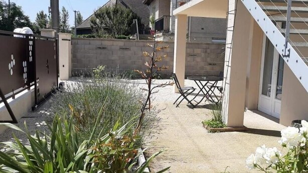 A residential backyard with a paved patio, a metal staircase, a small table, and a variety of plants.