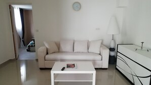 A minimalist living room with a white sofa, a coffee table, a lamp, and a sideboard.