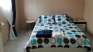 A bedroom with a bed, a bedside table, a nightstand, a hanging light fixture, and a window with curtains.