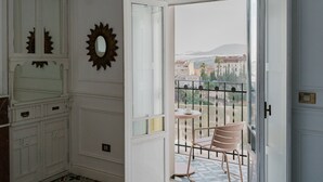 Quarto com uma grande janela, uma cadeira e vista para edifícios e montanhas.