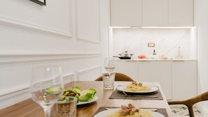 Uma mesa de jantar com pratos de massa e salada, copos de água e uma cozinha ao fundo.