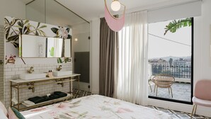 Ein Hotelzimmer mit einem großen Bett, einem Badezimmer mit Waschtisch, einem Balkon mit einem Sessel und Blick auf die Stadt.