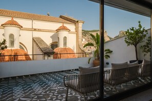 En balkon med et mønstret gulv, et siddeområde med stole og udsigt til en bygning med kuppeltoppe.