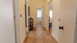 Un estrecho pasillo con suelo de madera, paredes blancas y una puerta a la derecha.