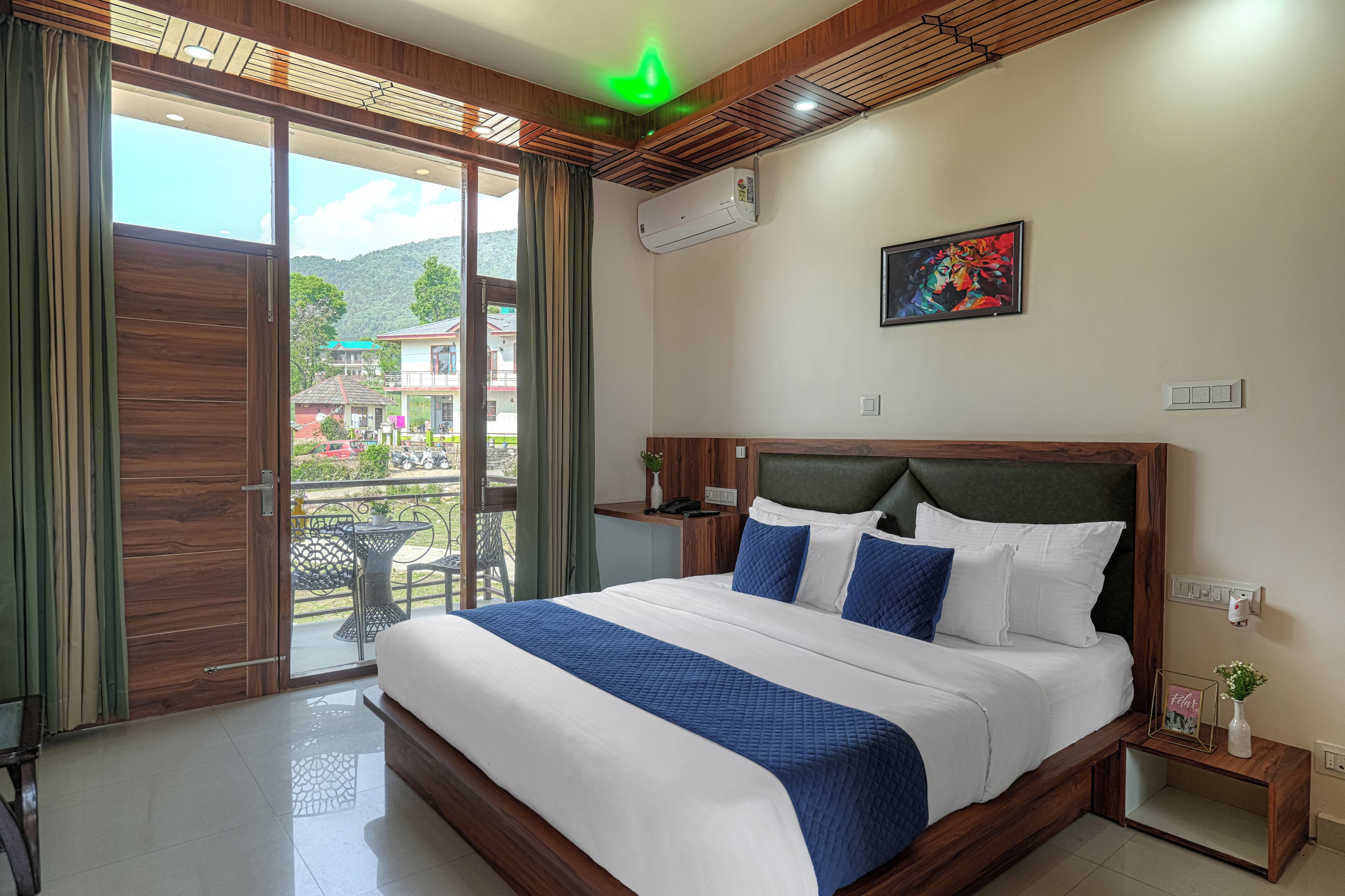 A hotel room with a large bed, a balcony with a table, and a painting on the wall.
