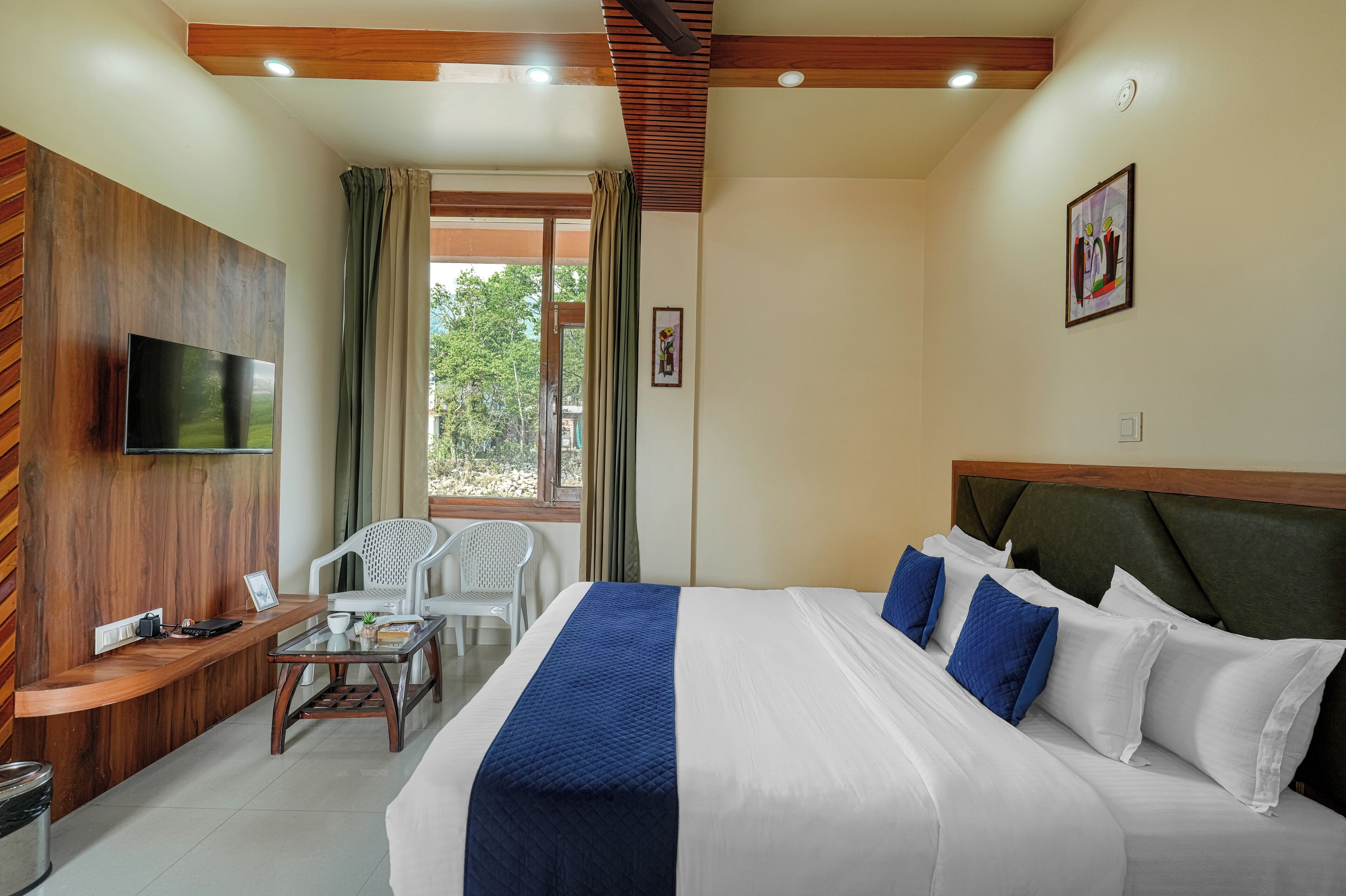 A hotel room with a bed, a TV mounted on the wall, a desk with a chair, and a window with curtains.