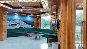 A modern interior with a green sofa, a wooden ceiling, and a large mural of a snowy mountain. - Appas Hotel (Baijnath)