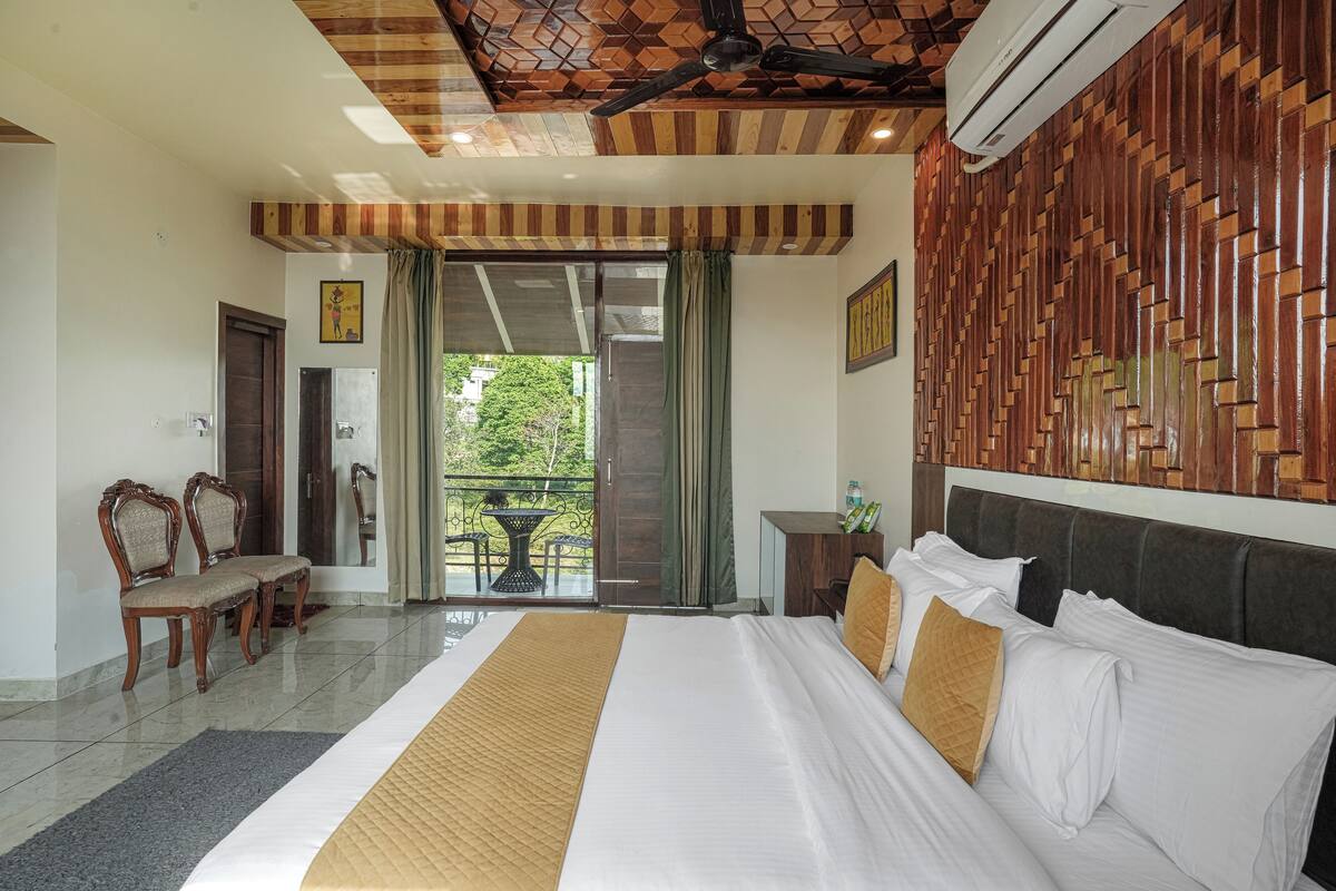 Habitación de hotel con una cama grande, techo de madera y un balcón con mesa y sillas.