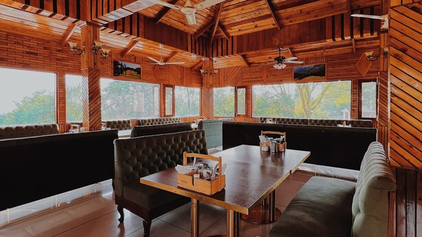 A wooden interior with a high ceiling, a dining table, and seating areas. - Appas Hotel (Baijnath)