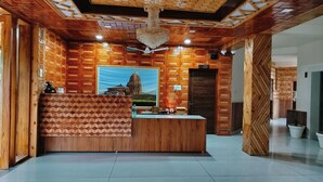 A reception area with a wooden reception desk, a large framed picture of a temple, and a sign indicating the location of the toilet. - Appas Hotel (Baijnath)