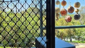 Vista a través de una ventana con un patrón de rejilla hexagonal, mostrando un edificio con techo azul y decoraciones esféricas colgantes.