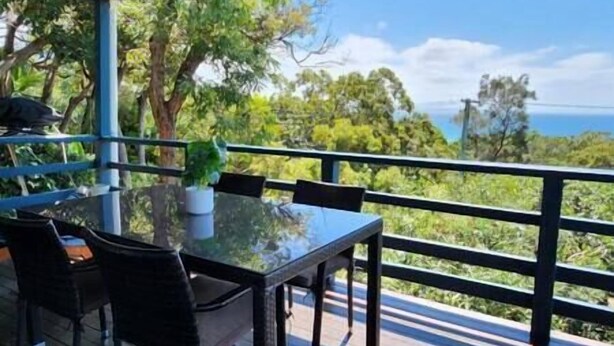 Un área de comedor al aire libre con una mesa y sillas de vidrio, con vistas a un paisaje escénico con árboles y vista al mar.