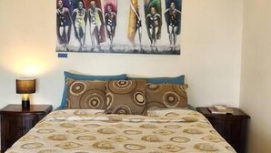 Un dormitorio con cama, mesita de noche, lámpara y un cuadro en la pared.