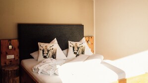 A neatly made bed with two pillows featuring a cow design, a wooden headboard, and a small wooden nightstand with a power outlet. - Thanks to its location in the southwest corner, a panoramic king with 56 m².
 (Sankt Gallenkirch)