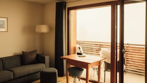 A room with a sofa, a table, a lamp, and a view of a balcony with wooden blinds. - So small and already 2 balconies, here the bedroom and living room with balcony. (Sankt Gallenkirch)