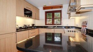 A modern kitchen with wooden cabinets, a black countertop, and a window with a view of greenery. - Lodge 22 Cherry (Wadebridge)