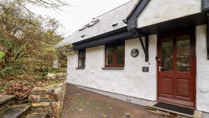 A white building with a brown door and windows, stone steps, and a paved area. - Lodge 22 Cherry (Wadebridge)