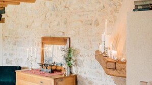 Ein rustikaler Raum mit Steinwand, Holzbalken, einem Schminktisch mit Spiegel und Kerzen auf einem Regal.