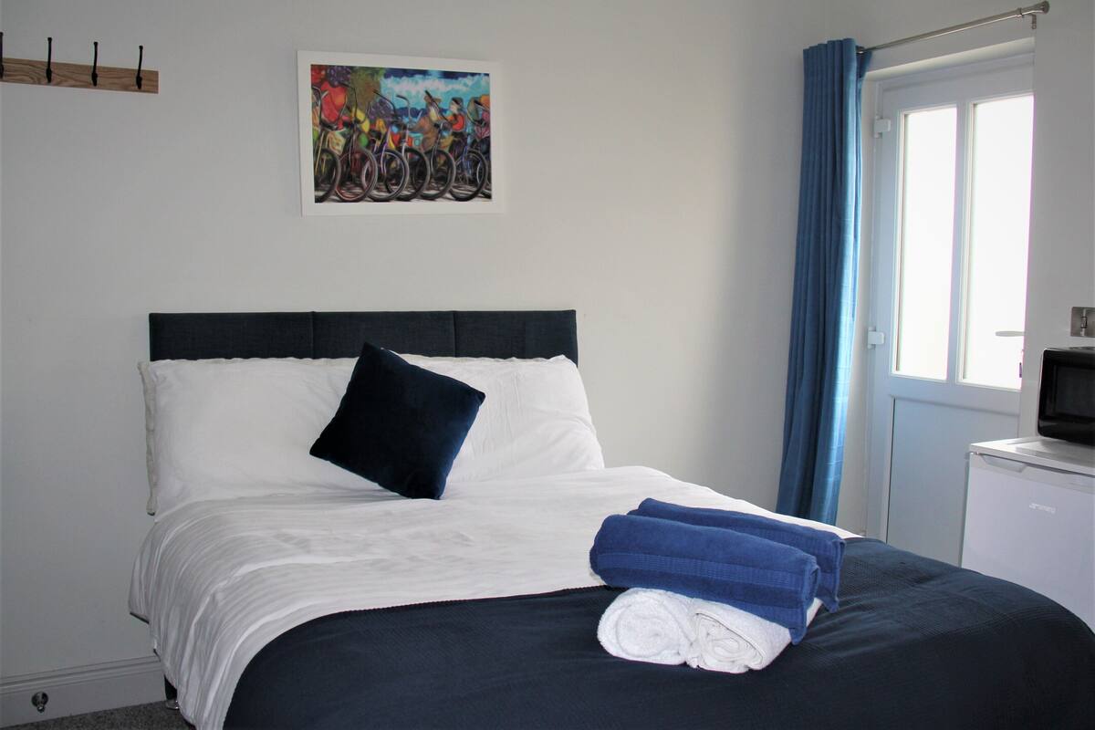 A neatly made bed with white and navy bedding, a black headboard, and a blue towel.