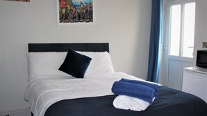 A neatly made bed with white and navy bedding, a black headboard, and a blue towel. - The Old Bike Shop Accommodation (Norwich)