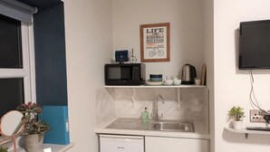 A compact kitchen with a microwave, coffee maker, and a small refrigerator. There's a sink with a faucet and a countertop with a potted plant. - The Old Bike Shop Accommodation (Norwich)