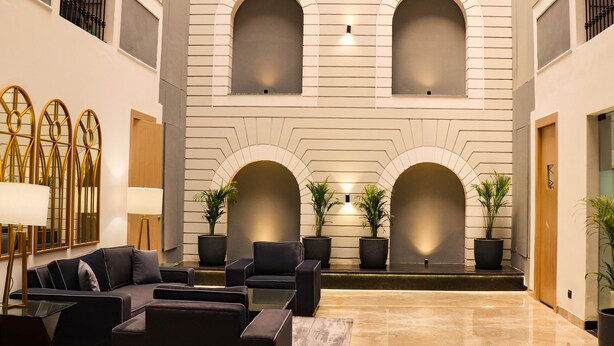 A spacious lobby with a modern design, featuring a seating area with sofas and armchairs, a large mirror, and potted plants. - Ahuja Residency Mayfield Garden (Gurugram)