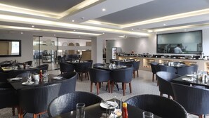 A modern hotel dining area with black wicker furniture, a bar, and a large TV screen. - Ahuja Residency Mayfield Garden (Gurugram)