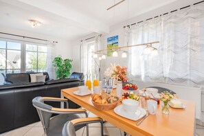 A modern kitchen with a dining area, featuring a wooden table set for breakfast, a black leather sofa, and a view of the outdoors. - Villa Cölpin Wohnung Stranddistel - Zentral und Strandnah Gelegen (Kölpinsee)