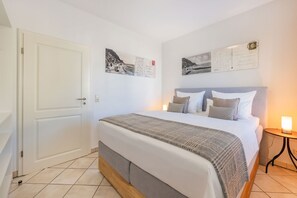 A bedroom with a bed, pillows, a bedside table with a lamp, and wall-mounted pictures. - Villa Cölpin Wohnung Stranddistel - Zentral und Strandnah Gelegen (Kölpinsee)
