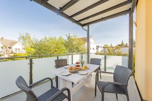A balcony with a table set for two, wicker chairs, and a glass railing. - Villa Cölpin Wohnung Stranddistel - Zentral und Strandnah Gelegen (Kölpinsee)
