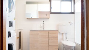 A modern bathroom with a wooden vanity, a toilet, and a washing machine.
