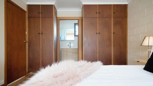 A bedroom with a large bed, wooden wardrobes, a fluffy pink rug, and a nightstand with a lamp.