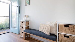 Um quarto com porta azul, um banco com cestos de armazenamento e uma pequena mesa com um vaso.